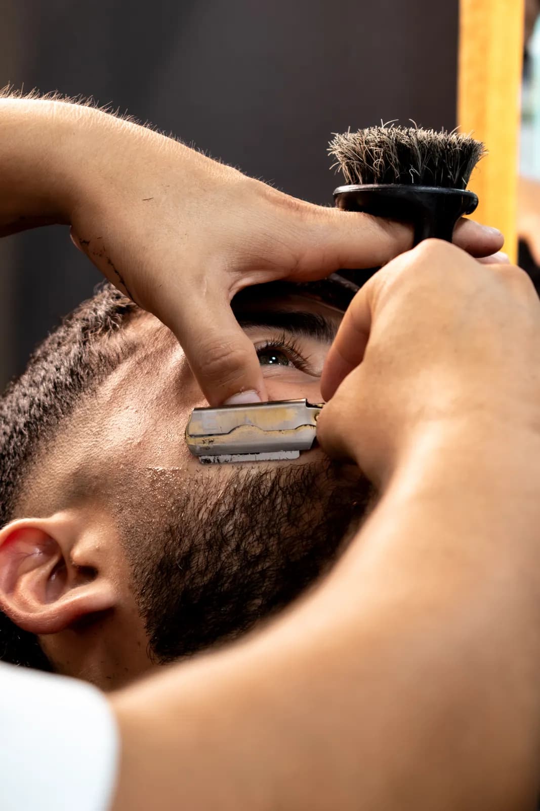 Barbero perfilando la ceja de un cliente con navaja