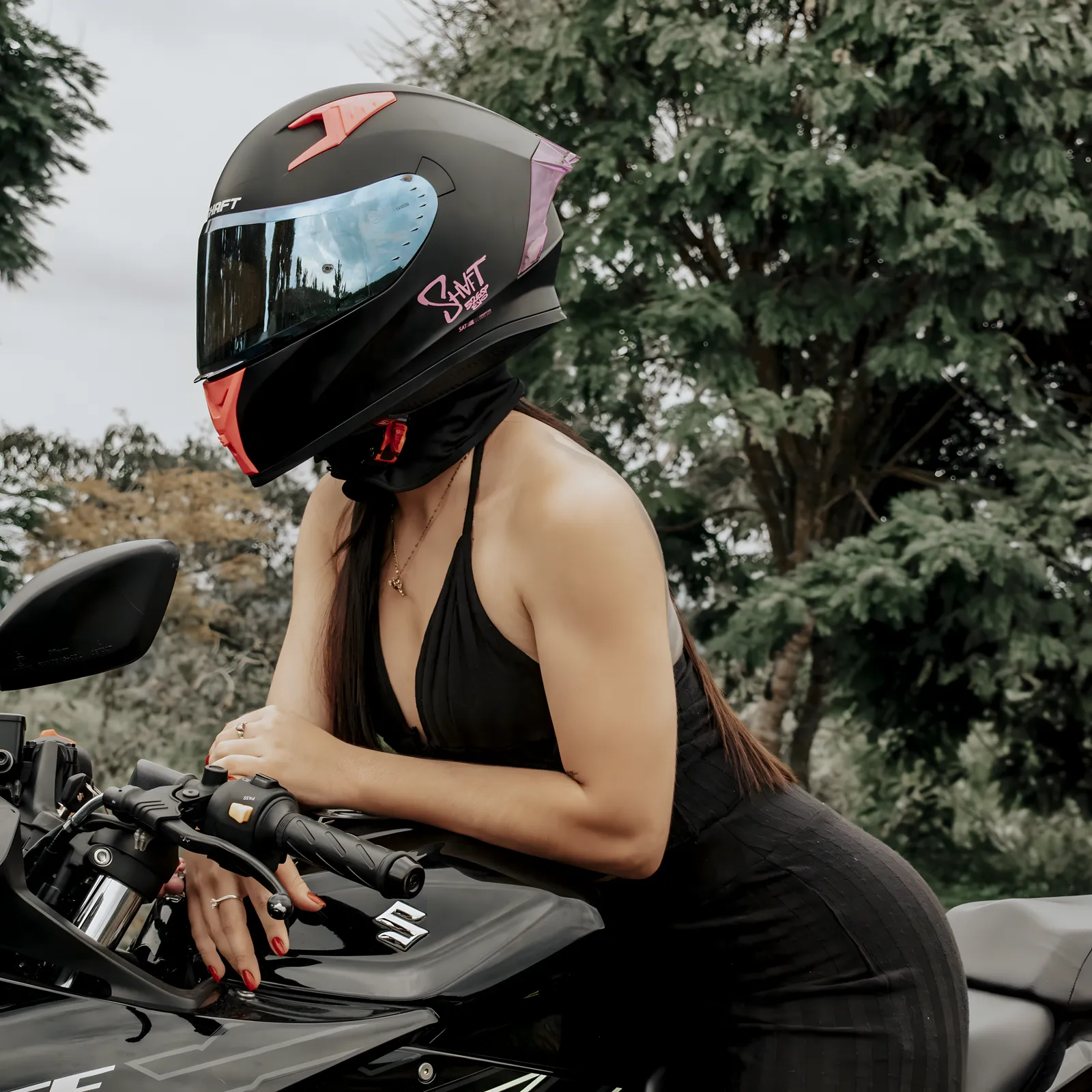 Mujer con casco posando sobre una motocicleta deportiva entre árboles