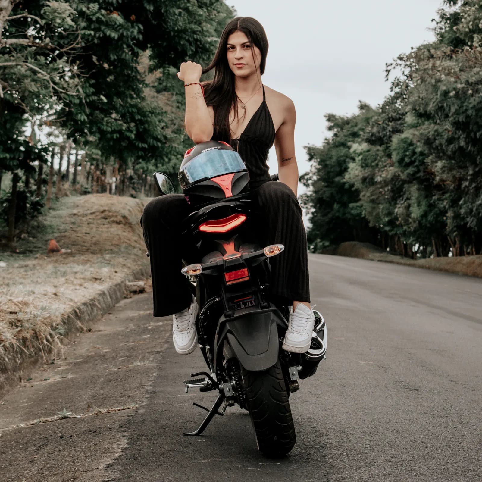 Mujer posando de pie junto a una motocicleta en una carretera rural