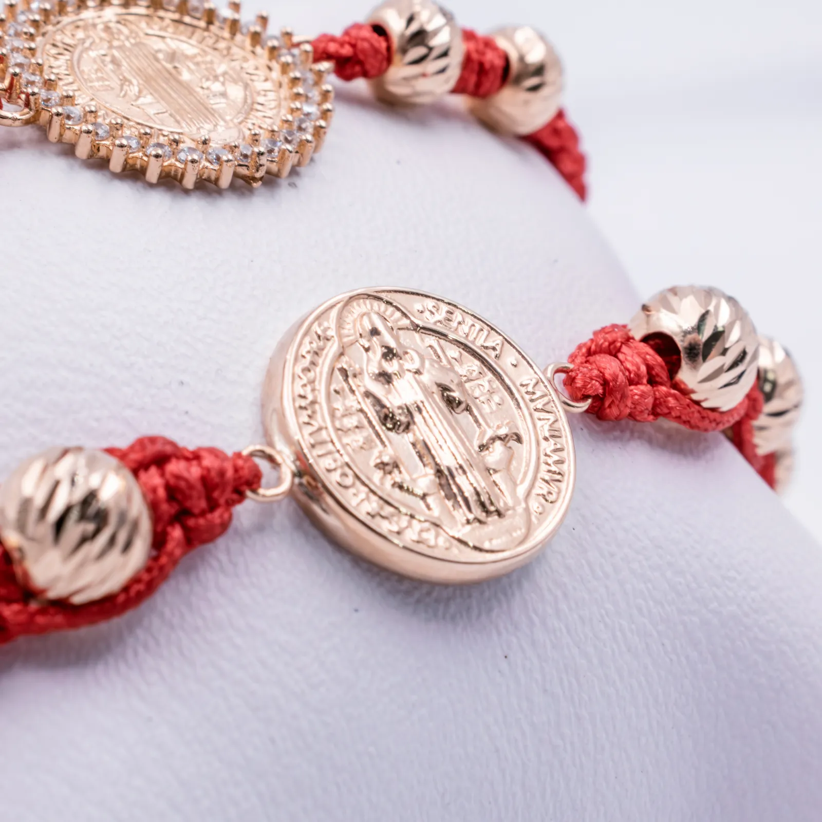 Detalle de pulseras rojas tejidas con medallas doradas de San Benito