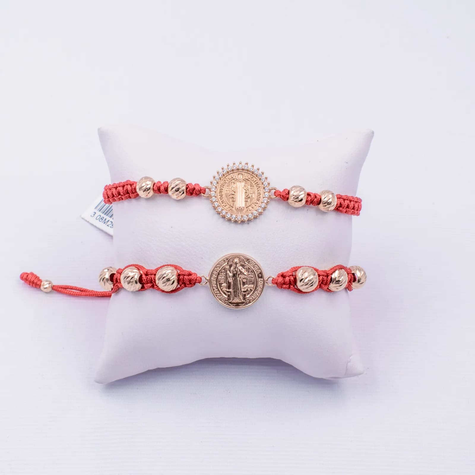 Dos pulseras rojas con medallas doradas exhibidas sobre una almohadilla blanca