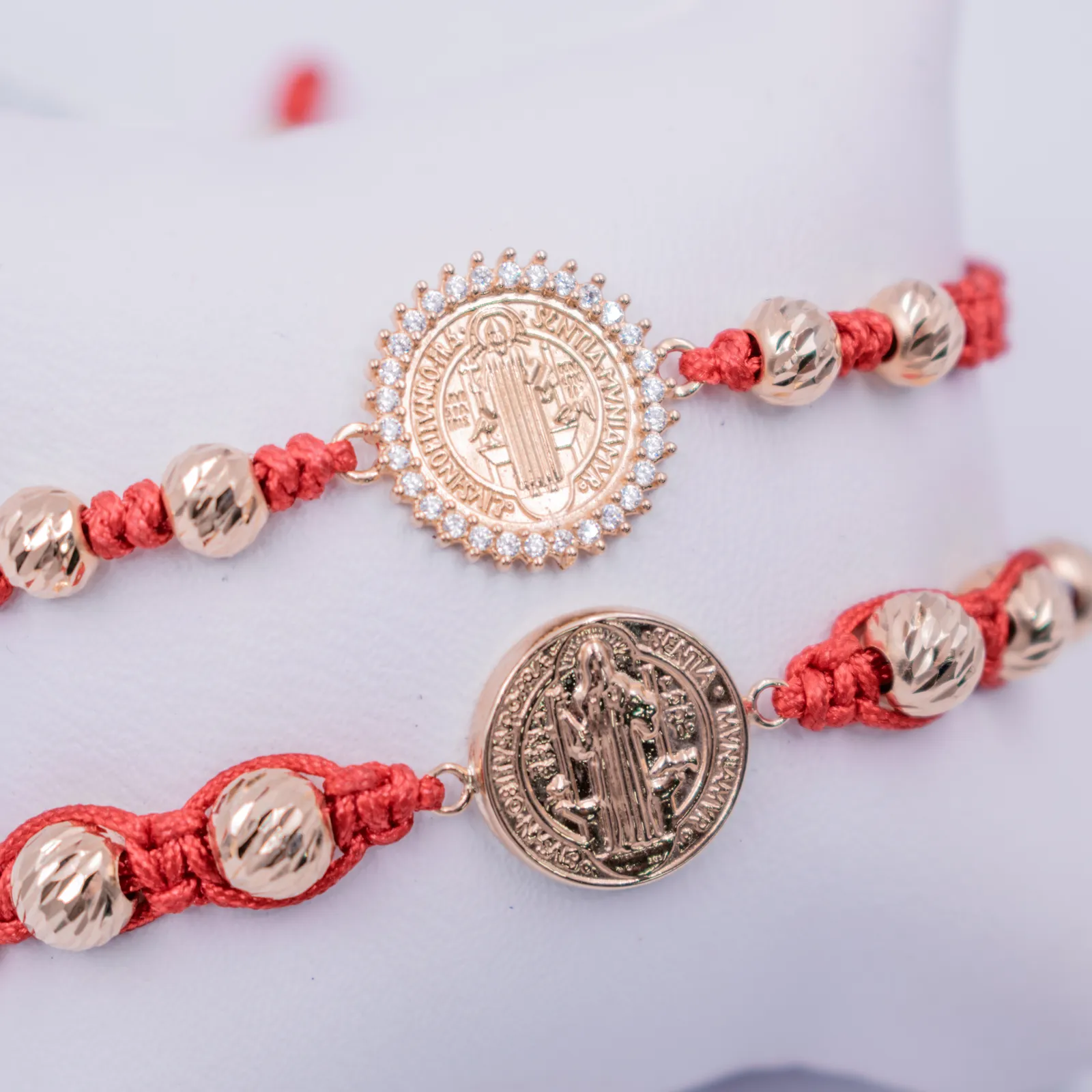 Pulseras rojas con medallas de San Benito en oro sobre fondo blanco
