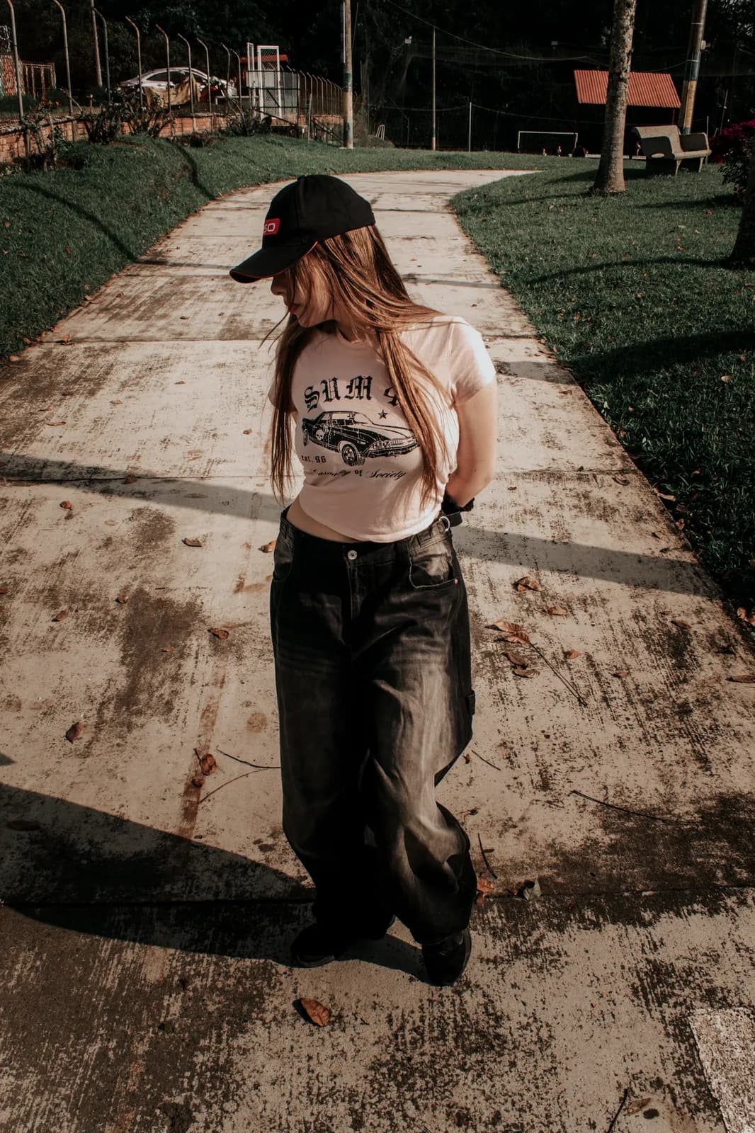 Joven con gorra posando en un sendero de concreto entre jardines
