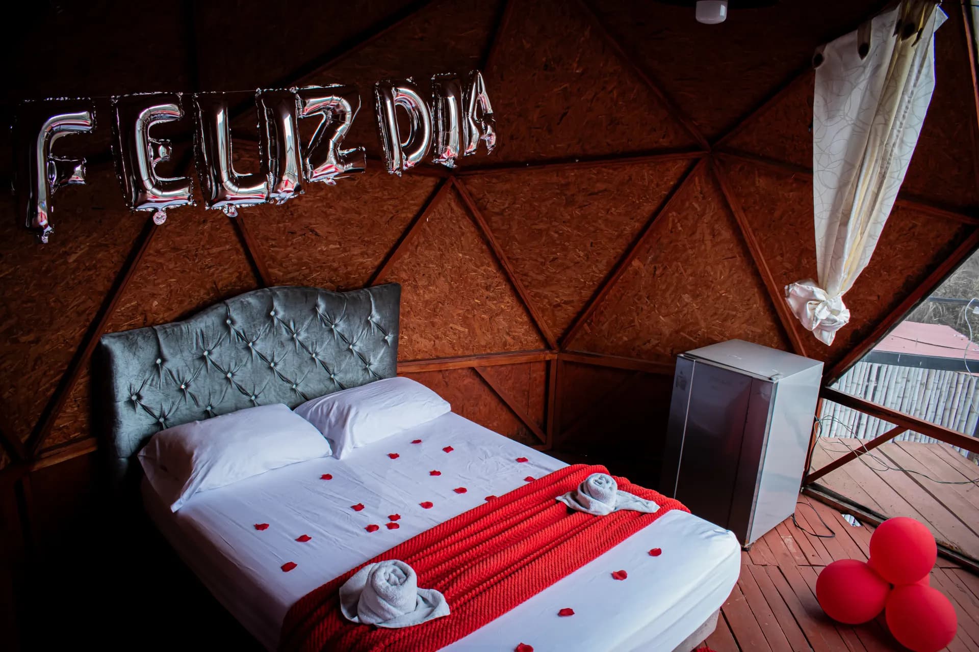 Interior de domo de glamping con cama decorada con pétalos y globos